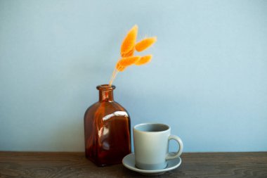 Gri kahve fincanı, ahşap masada portakal çiçeği vazosu. mavi duvar arkaplanı