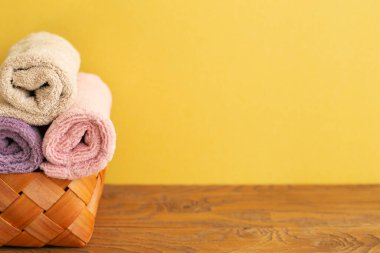 Tahta masadaki sepetteki banyo havluları. Sarı arka plan. Boşluğu kopyala