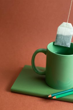 Green object. Cup of tea, notebook, colored pencil on red background. workspace