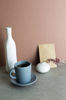 Still Life of coffee cup and envelope and ceramic vase with dry plant. gray background