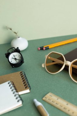 Various office supply stationery. notebook, glasses, pencil, ruler, clock, plant on green desk background
