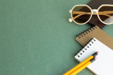 Various office supply stationery. notebook, glasses, pencil on green desk background with copy space