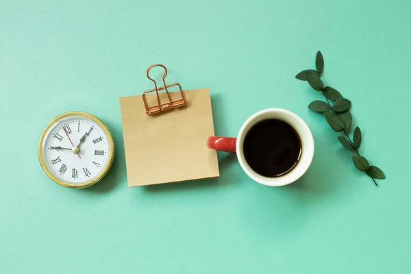 Notepad, clock, cup of coffee, green leaf on mint green background. office desk, workspace. top view
