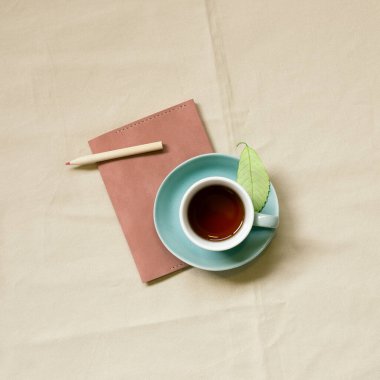 Günlük not defteri ve bej kumaş arka planda bir fincan kahve. Üst görünüm, boşluk kopyala