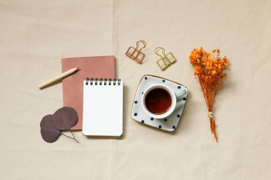 Not defteri, kalem, kahve fincanı, şarjör, bej kumaş arka planda kuru çiçekler. Üst görünüm, boşluk kopyala