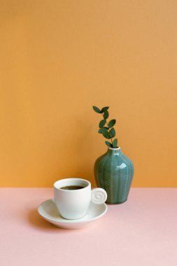 Pembe masada yeşil yapraklı beyaz kahve fincanı. turuncu duvar arka planı. Boşluğu kopyala