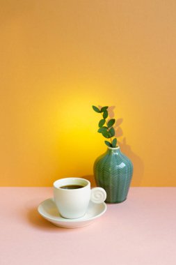 Pembe masada yeşil yapraklı beyaz kahve fincanı. turuncu duvar arka planı. Boşluğu kopyala