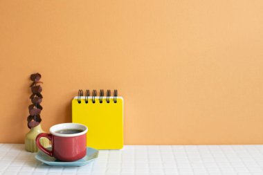 Bir fincan kahve ve not defteri, beyaz masada kuru okaliptüs. turuncu duvar arka planı. Boşluğu kopyala