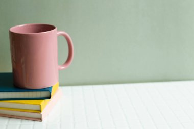 Pembe bardak ve defter beyaz masada. haki yeşil duvar arkaplanı