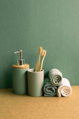 Sabun, şampuan şişesi ve pamuk havlu, kahverengi rafta diş fırçası. Yeşil duvar arkaplanı. banyo içi