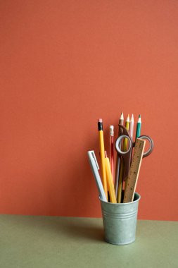 Haki masasında kalem tutacağı. Kırmızı duvar arkaplanı. Çalışma alanı, ofis malzemesi