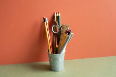 Haki masasında kalem tutacağı. Kırmızı duvar arkaplanı. Çalışma alanı, ofis malzemesi