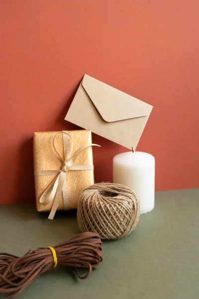 Gift box and wrapping roll, envelope, candle on khaki table. red wall background. anniversary, birthday, christmas, greeting concept