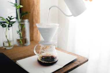 Odadaki masaya damlayan kahvenin üzerine sıcak su dökmek.