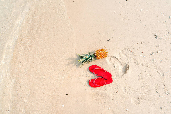  pineapples and red flip flops on the beach.