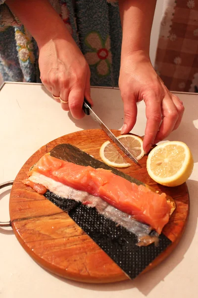 Hand schneidet Scheiben von rotem Fisch und Zitrone — Stockfoto