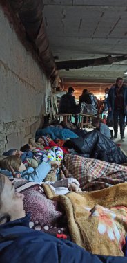 Chernihiv - Ukraine. 01 March 2022: shelter filled with group of people sitting on floor by sleeping bags. People sleep in a bomb shelter in Chernihiv during the bombardment of the city by Russian troops.