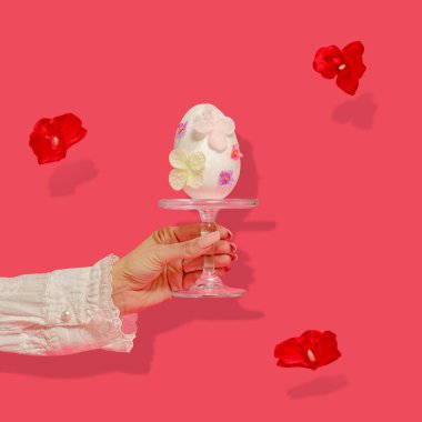 Yaratıcı Paskalya soyut kavramı. Dişi bir el büyük beyaz bir Paskalya yumurtası tutuyor. Yumurta pastel çiçeklerle süslenmiştir. Gölgeli kırmızı çiçekler hareket halinde. Paradise Pembe arka plan hakkında dinamik bir fikir