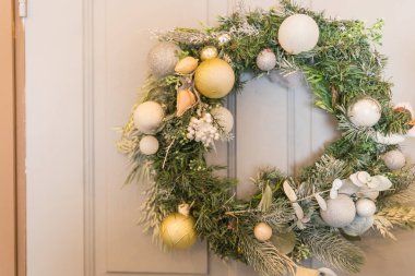 Altın, beyaz toplar, ışıklar ve çam kozalaklarıyla süslenmiş yeşil Noel çelengi eski, ahşap bir arka planda, rustik tarzda. Kış tatili için el yapımı bir çelenk..