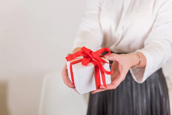 Девушка в белой рубашке с белой подарочной коробкой с красным бантом на размытом фоне. Праздники на Рождество, Новый год, день рождения. — стоковое фото