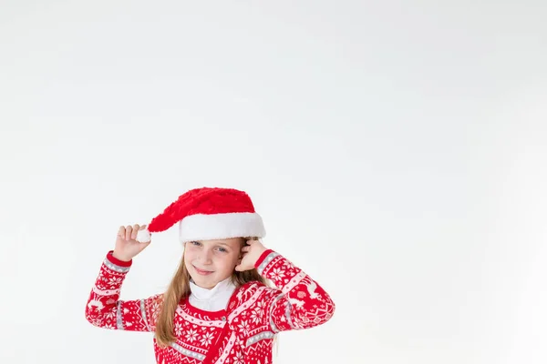 Retrato de niña feliz bailando, vistiendo suéter de navidad roja y sombrero de santa aislado sobre fondo blanco. Joven caucásico alegre sonrisa rubia chica en un suéter de ciervo rojo de Navidad es feliz. —  Fotos de Stock
