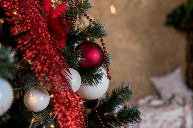 Süslü bir Noel dalına asılı kırmızı ve beyaz takılar. Odaklanamayan ışıklarla soyut bir arkaplan. Yeni yıl ve Noel için dekore edilmiş bir oda..