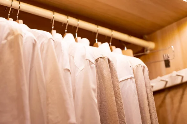Hangers with different clothes in wardrobe closet.shirts and dress hanging on rail in wooden wardrobe. minimalistic modern scandinavian white wood walk in closet with wardrobe in neutral beige colors — Stock Photo, Image