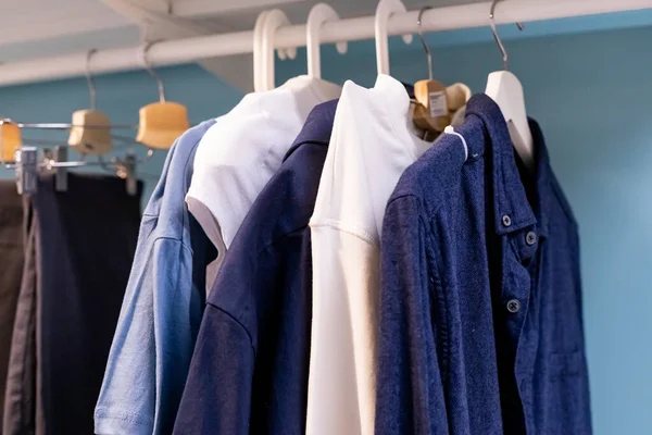 Cabides com roupas diferentes no armário do guarda-roupa. camisas brancas e azuis estão penduradas no trilho em guarda-roupa de madeira em casa. — Fotografia de Stock