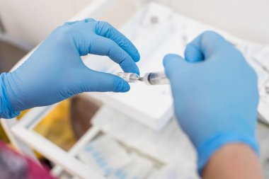 Şırıngalı doktor iğne yapmaya hazırlanıyor. Doktorların elleri şırınga ve şişeyle. Sıvı ilaç ya da tedavi için aşı, hemşirenin elinde grip. COVID-19 koronavirüs aşısı kavramı.