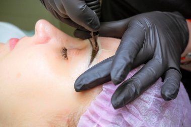 Kozmetik uzmanı kaşlara kalıcı makyaj uyguluyor. Seçici odaklanma ve alanın sığ derinliği. Mikrobleying kaşları güzellik salonunda çalışıyor.