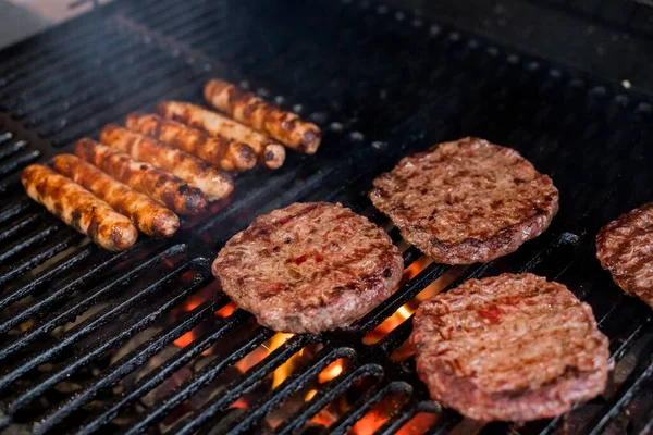 Rauchiges Hamburger-Fleisch-Grillen für Burger. Auf dem Grill am offenen Feuer braten - BBQ. Burger und Würstchen auf dem Grill. Stockbild