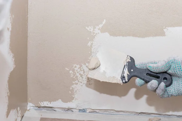 Mann verputzt Wand mit Spachtelmesser, Vorbereitung für Anstrich.Hände des Arbeiters mit Putzwerkzeugen renovieren Haus. Putzer saniert Wände und Ecken mit Spachtel Stockfoto