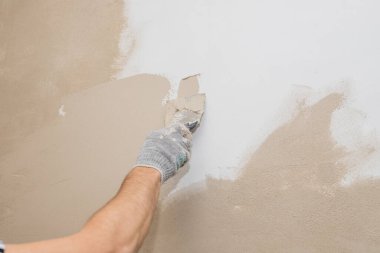 Duvarı macun bıçağıyla sıva yapan bir adam, boyama için hazırlanan bir adam. Duvarları sıva malzemesi ile kaplayan ve evi yenileyen bir işçinin elleri. Sıvacı, duvarları ve köşeleri spatula ile yeniliyor. Boşluğu kopyala
