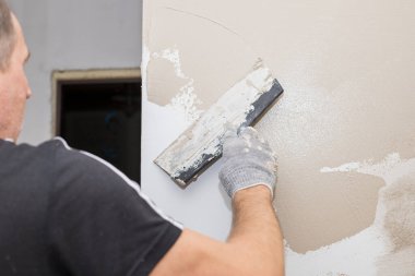 Duvarı macun bıçağıyla sıva yapan bir adam, boyama için hazırlanan bir adam. Duvarları sıva malzemesi ile kaplayan ve evi yenileyen bir işçinin elleri. Sıvacı, duvarları ve köşeleri spatula ile yeniliyor. Boşluğu kopyala