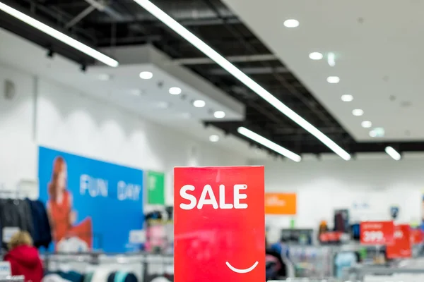 Um sinal com a inscrição VENDA em branco em um fundo vermelho no piso comercial da loja de roupas casuais. Conceito de moda, temporada de desconto, sexta-feira preta, compras offline, truques, vendas de férias. — Fotografia de Stock