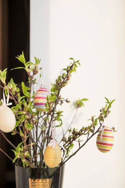 Composizione pasquale. rami di albero con piccole foglie verdi e uova di Pasqua colorate su sfondo sfocato.Concetto interior design per le vacanze di primavera — Foto Stock
