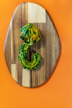 Tahta kesme tahtası ve turuncu arka planda ilginç şekilli yeşil ve sarı balkabağı resmi. 