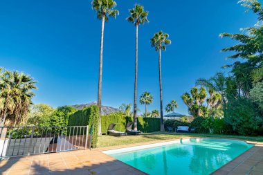 Marbella 'da bir villada havuz başında bir resim. Arkasında palmiye ağaçları ve dağlar var. 