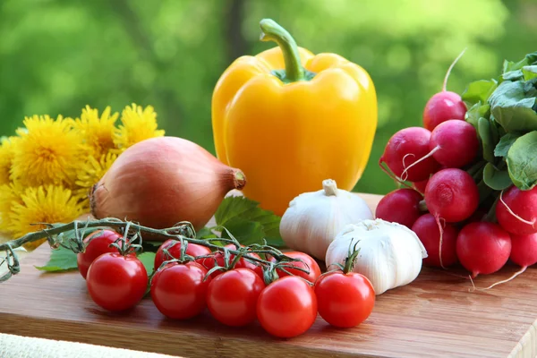 Uma coleção de verduras de primavera: tomates de cereja, alho, rabanete, cebola, pimentão em madeira decorada com flores de dente-de-leão — Fotografia de Stock