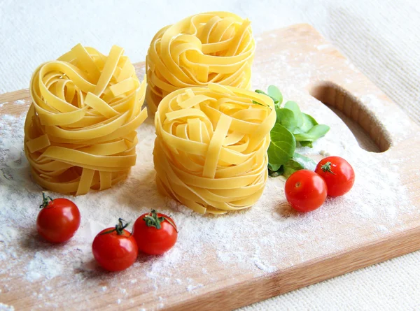 Composição feita em cores de bandeira italiana: três porções de macarrão tagliatelle cru, juntamente com tomates cereja e ervas em uma tábua de corte — Fotografia de Stock