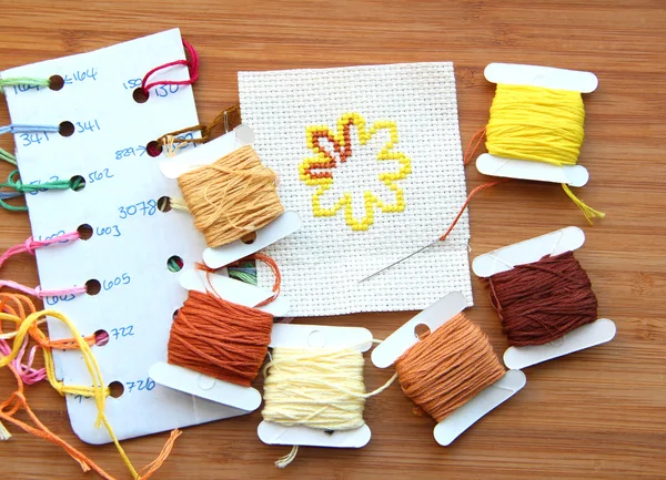Cross-stitch set: colour palette, threads, canvas against a wooden background — Stock Photo, Image