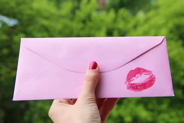 Mano femenina sosteniendo un sobre rosa con un lápiz labial rojo beso impresión y espacio de copia — Foto de Stock