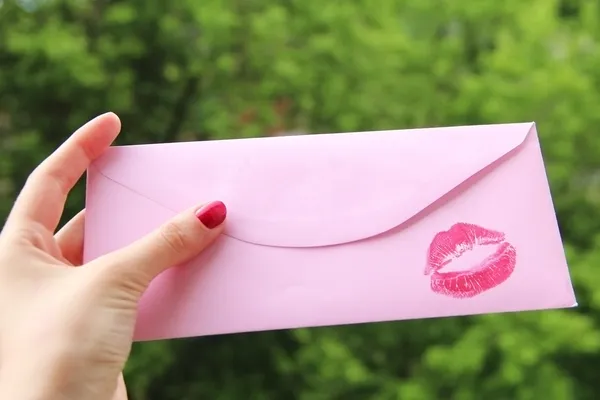 Female hand holding a pink envelope with a red lipstick kiss print and copy space — Stock Photo, Image