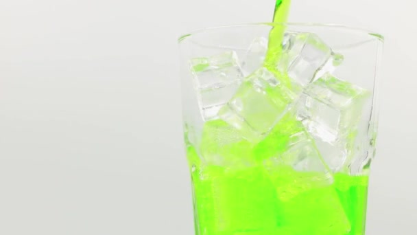 氷のキューブを閉じると緑の輝く水を入れてください 氷をガラスにした緑色の輝く水 白い背景に緑の輝く水を飲むの回転ガラス — ストック動画