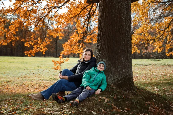 Matka a syn sedí v podzimním parku pod stromem — Stock fotografie