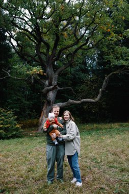 Mutlu bir aile bir çocukla yürüyüşe çıktı. Annem ve babam parkta yürürken bebeği kollarında tutuyorlardı.