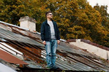 Çatıda bir adam duruyor. Gözlüklü genç bir adam evin eski demir çatısına bakıyor..