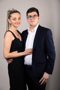 the couple looks into the camera against the background of a gray wall