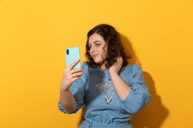 Telefonu olan bir kadın sarı arka planda selfie çekiyor..