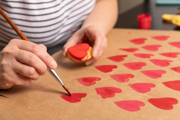 Sello de patata en forma de corazón en papel artesanal. El proceso de decorar un regalo para el Día de San Valentín. Preparándose para la celebración del 14 de febrero. — Foto de Stock